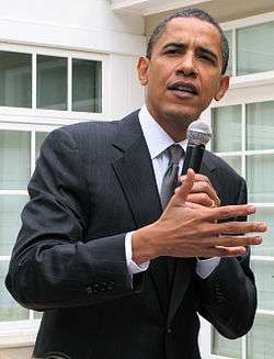 Picture of a man holding a microphone and talking and gesturing.
