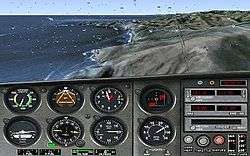 The top half of the image is the view out of a rain-specked airplane windshield, through which a coastline is visible. The bottom half features numerous flight instruments, such as an altimeter and a variometer.