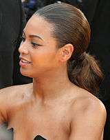 Beyoncé Knowles facing to the left, with her hair tied back, and wearing a strapless black dress.