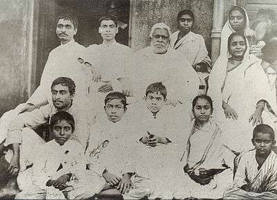 A group photograph of a large Indian family seated in rows around an old grey-haired man.
