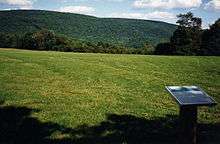 A green mountain in the background with a grassy hill and a sign in the foreground