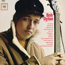 A close-up of Bob Dylan wearing a coat and hat, holding a guitar