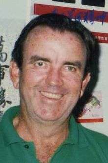 Middle-aged man wearing a green polo shirt, with brown hair combed back, smiling.
