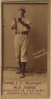 A black and white baseball card featuring a man in a white baseball jersey and striped cap holding both hands out cupped in front of his chest.