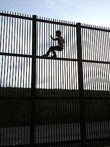 "Wildlife-friendly" border wall in Brownsville, Texas, which would allow wildlife to cross the border. A young man climbs wall using horizontal beams for foot support.