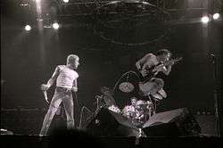 Roger Daltrey holding a microphone and Pete Townshend jumping on stage