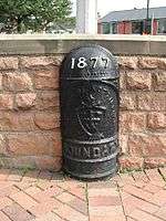 A black cast-iron hald-round post with a domed top. Around one metre high. It has the year ‘1877’ in white raised lettering. It also says ‘CITY OF NOTTINGHAM’ in capital letters which is accompanied with the coat of arms of the City of Nottingham, and the word ‘BOUNDARY’ in capital letters below that.