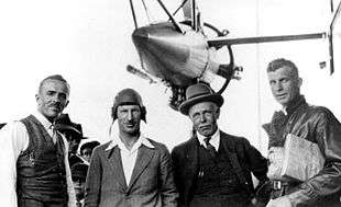 Half-length informal portrait of four men with an aircraft engine and struts above and behind them