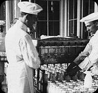 Two men in white, one arranging milk bottles