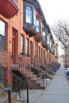 A view down a city sidewalk with identical orange brick rowhouses, all with a projecting upper window