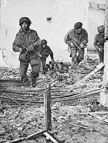 Four men in a bomb damaged building, with debris on the ground