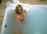 A blond woman in a bathtub. She is looking at her hand covered in blood.