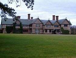 A long two-storey house with five gables, almost entirely timber-framed.  In front is a large expanse of lawn.