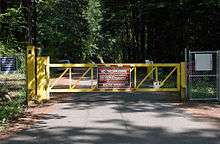 A gate and fence block a forest road. Lettering on a warning sign on the gate says in part, "No Trespassing: Bull Run Watershed"