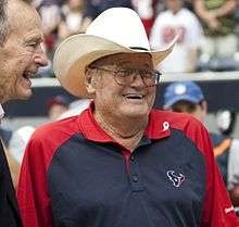 Photograph of a laughing Phillips wearing a Houston Texans polo shirt standing beside former U.S. President George H. W. Bush