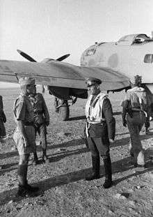 four men in military uniforms standing in front of a propeller driven aircraft