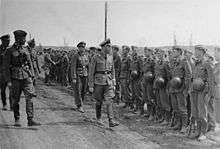 a black and white photograph of a bespectacled Heinrich Himmler in uniform walking along a line of soldiers in Waffen-SS uniform