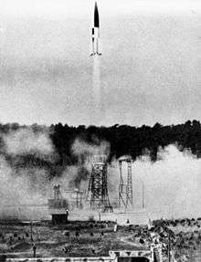 A black and white photograph showing the launch of a V-2 rocket; the rocket is twice its own height from the launchpad, which is partially obscured by clouds of smoke