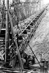 A single Hochdruckpumpe barrel mounted on the side of a steep wooded hill, with flights of steps on each side of it and machinery in the foreground