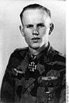 A man wearing a camouflage military uniform with an Iron Cross displayed at the front of his uniform collar.