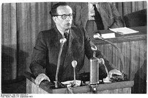 A man with glasses talking into microphones behind a lecturn.