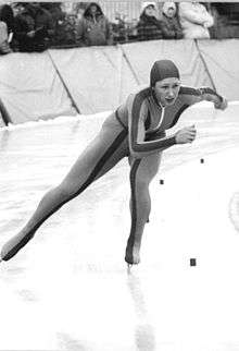 A woman wearing a hooded unitard speed-skates along an ice track.