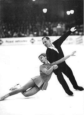 Two people are in a figure skating spin, the man is upright on the left, spinning the woman around himself.