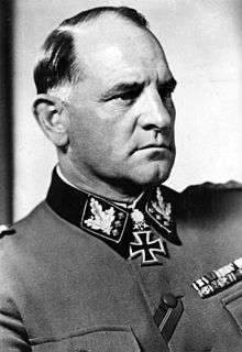 A man in semi profile wearing a military uniform and neck order, in the shape of a cross. He has short, thinning hair and a determined facial expression.