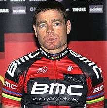A man in his mid thirties wearing a black and red cycling jersey with white trim, and notable rainbow stripes around the biceps.