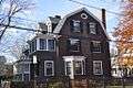 A large brown 3 story colonial style house with white trim and black shutters.