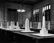 Approximately a dozen monument models sit on tables in a stone walled room.