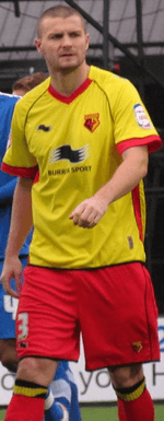 A man wearing a yellow shirt, red shorts and red socks