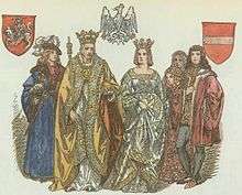 An elderly man wearing a crown, with a crowned woman on his left, surrounded by two young men and two young women