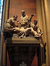 Small stone statuary, mounted on a wall, depicting the crucifixion of Jesus