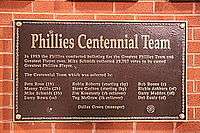 A dark bronze plaque listing the names and positions of members of the Centennial team in gold lettering