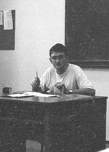 Cezary Geroń on a badly damaged black and white photograph, shown seated behind a teachers' desk.