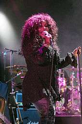 A woman is performing on stage. She wears a dark sweater and metallic-colored jeans.