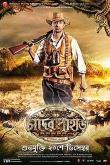 An young man of Indian origin is looking back with a rifle on his shoulder, having a backdrop of jungle, animals, mountain ranges and the logo art of the film