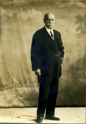 Full-length sepia portrait of distinguished gentleman with sideburns, wearing a 3-piece suit; body slight left-tilt