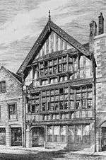 A black-and-white drawing of a three-storey timber-framed building seen from an angle. The lowest storey has a door on the left with a series of windows to the right; glazing extends across the middle storey, with a wide oriel window in the centre; the top gabled storey also contains an oriel window and at the top is an elaborately carved bargeboard.