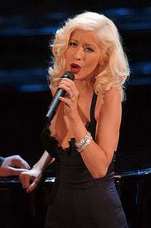 A blond woman singing, wearing a black gown