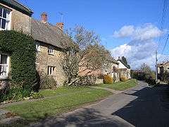A line of cottages, some thatched, along a road.