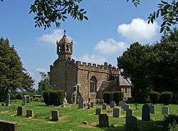 Stone building with small bell tower. In the foreground are gravestones.
