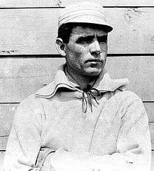 Medium black and white photo of white man with dark hair, mostly in profile, wearing an old fashioned baseball cap and uniform shirt