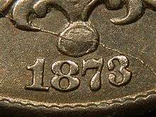 A closeup of part of an 1873 Shield nickel, showing the date, in which the arms of the "3" reach close to each other