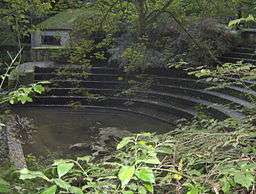 Semicircular stone steps, partially obscured by trees. Water to the left