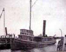 A small steamship sits at dock, mast and smokestack visible and the cabin facing front, with an almost identical boat on its right.