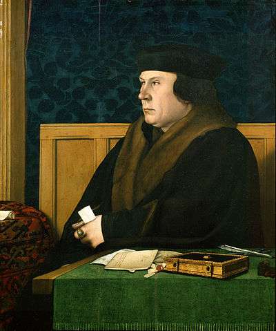 A Tudor man in a large coat and hat, possibly of fur, sitting at a desk