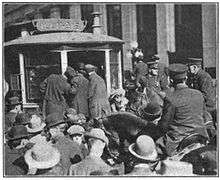A crowd of men swarm around a streetcar and mounted police officers