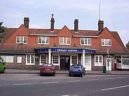A brown-bricked building with a blue sign reading "CROXLEY STATION" in white letters and three cars parked in front all under a blue sky with white clouds